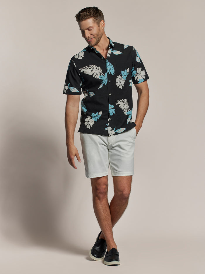 Black floral-print short-sleeve Hawaiian shirt with light shorts, standing front view.