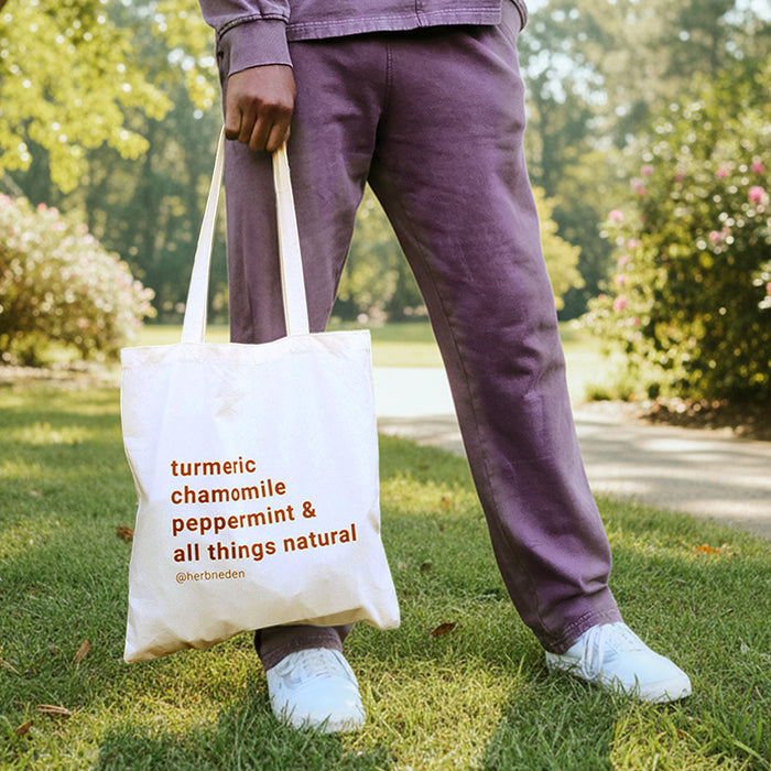 Person holding Herb'N Eden natural canvas tote bag with turmeric chamomile peppermint and all things natural design outdoors