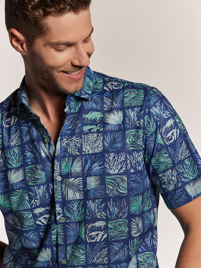 Blue and green leaf and ocean- grid print cotton lawn shirt, man looking down, three-quarter view.