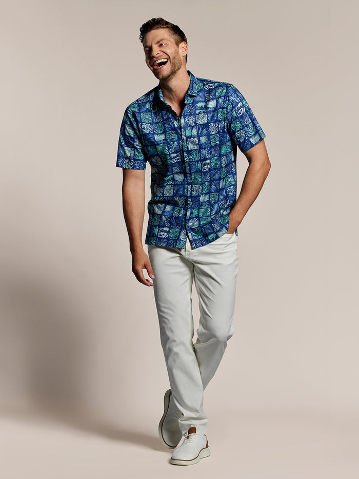 Blue and green leaf and ocean- grid print cotton lawn shirt, white pants, and shoes, front view on beige background.