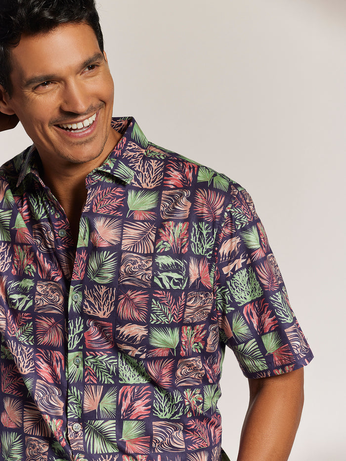 Red and mint green tropical leaf and coral-print cotton shirt, side view of model smiling man