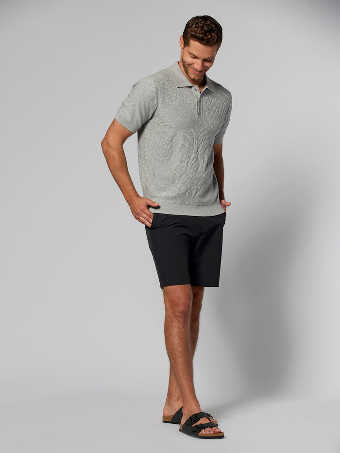 Light grey textured sweater polo, black shorts, sandals, front view, hands in pockets.