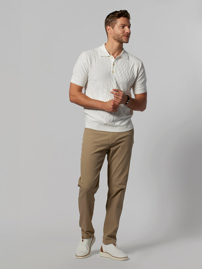 Man in white knit sweater polo, tan pants, and white shoes, front view.