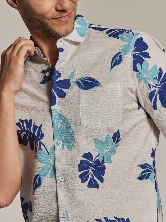 White short-sleeve shirt, blue/teal floral print, man touches collar. Close-up adjusting collar.