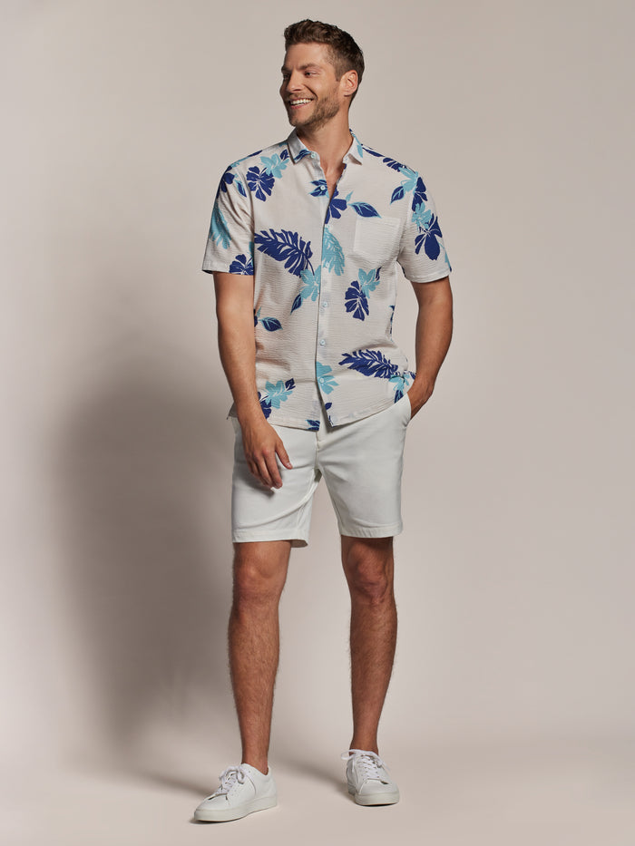 Blue floral-print short-sleeve shirt with light shorts and white sneakers, front view.