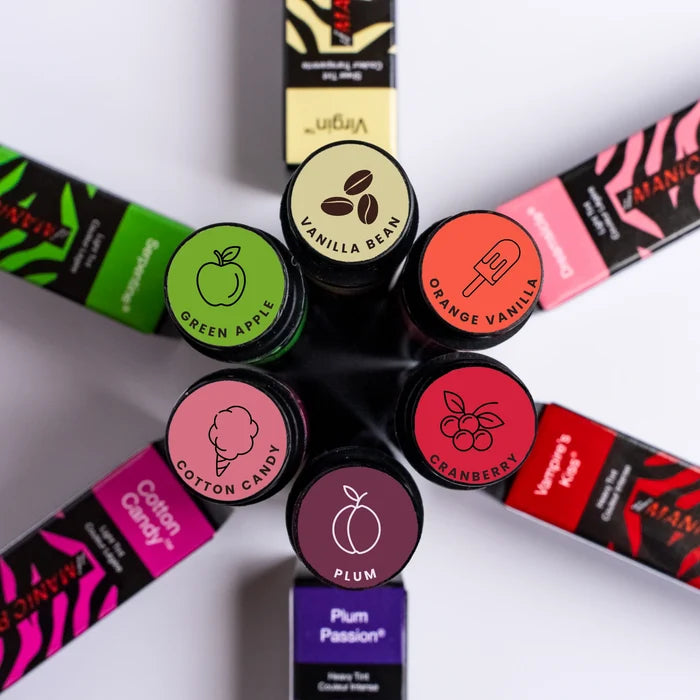 Manic Panic tinted lip balm flavors shown in flat lay with open balm sticks including green apple vanilla bean orange vanilla cranberry cotton candy and plum shades with sheer hydrating color