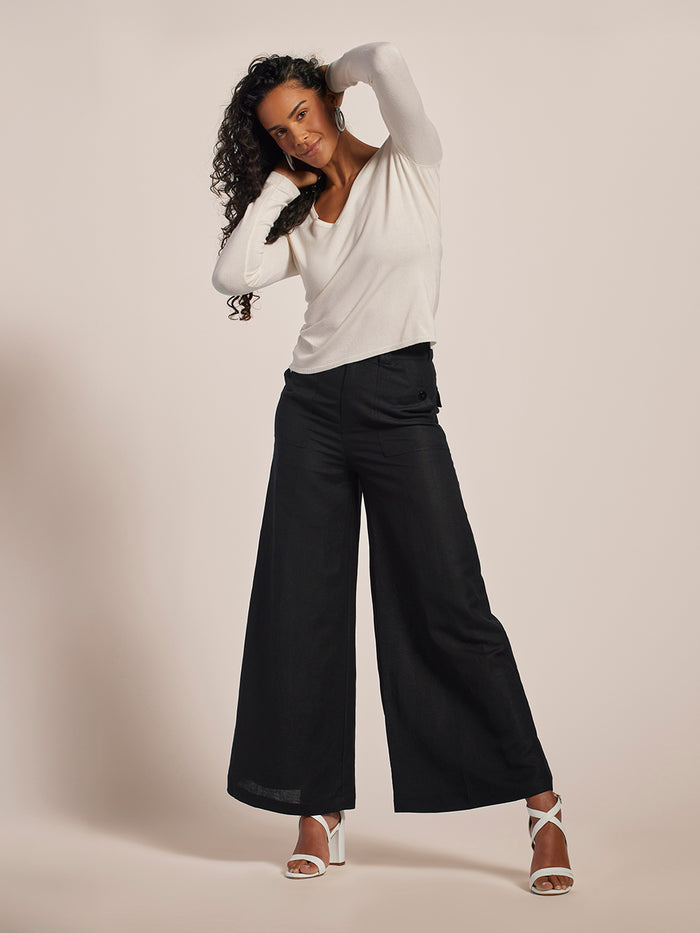 Woman wearing a white long-sleeve top and black wide-leg pants against a plain background
