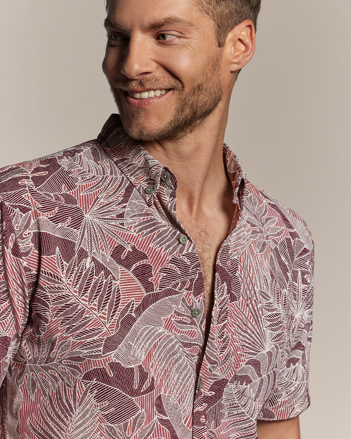 Maroon, pink, and white tropical-leaf print short-sleeve shirt, model looking left, upper body view.