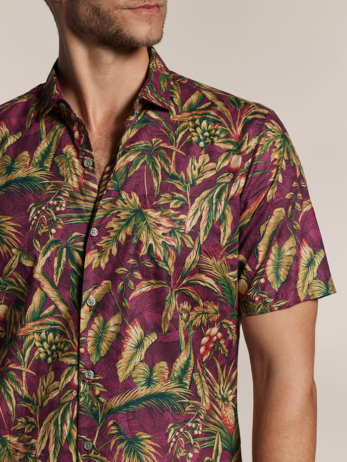 Maroon short-sleeve shirt with green/yellow tropical leaf print pattern, side view, head partially out of frame.