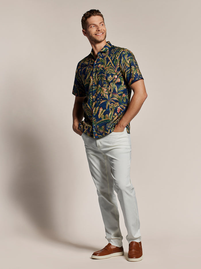 Green and brown tropical leaf-print cotton button-up- short sleeve shirt, paired with white pants, front view.