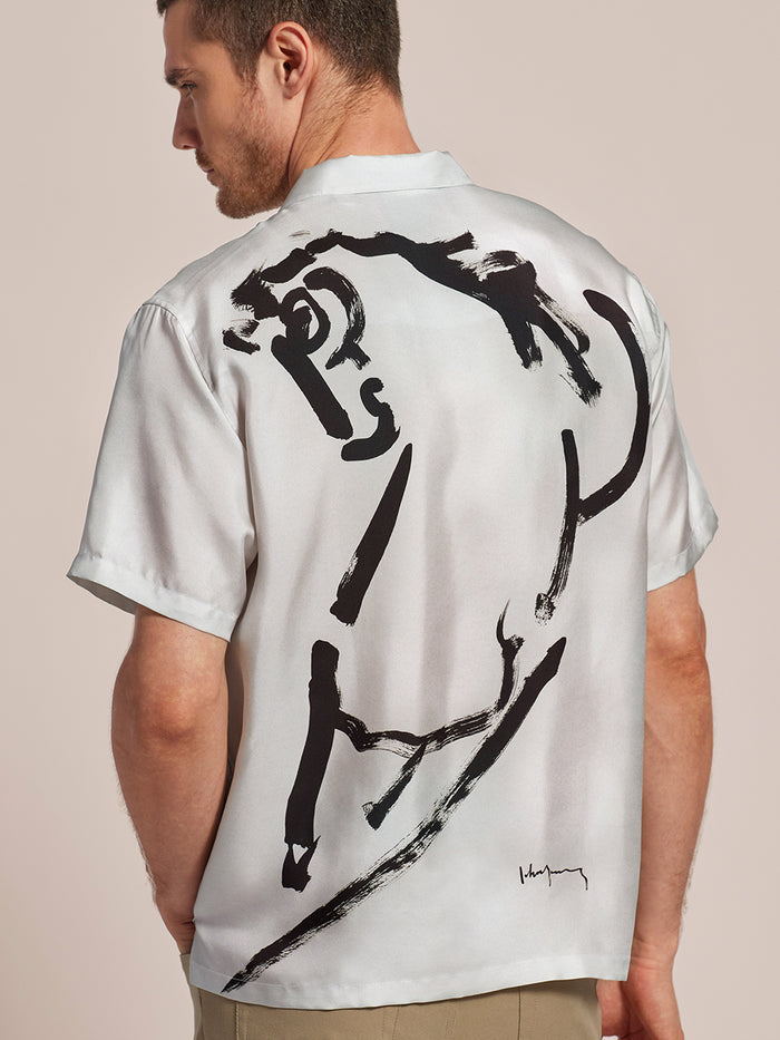 White shirt with black abstract face graphic, shown from the back on a man facing away.